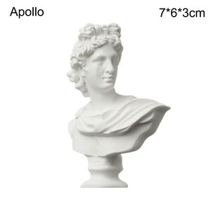 May include: A white bust of Apollo, a classical sculpture. The bust is 7 inches tall, 6 inches wide, and 3 inches deep. The sculpture features detailed facial features and draped fabric. The word "Apollo" is printed above the bust.