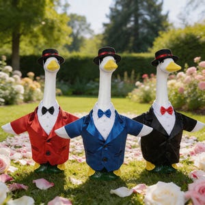 May include: Three goose figurines dressed in formal attire, including tuxedos in red, blue, and black, bow ties, and miniature black hats. The geese stand on green grass surrounded by rose petals and flowers.