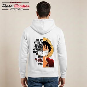 Puede incluir: Sudadera con capucha blanca con un gráfico de Monkey D. Luffy de One Piece. El diseño presenta la cara de Luffy y el texto "I'VE SET MYSELF TO BECOME THE KING OF PIRATES AND I DIE TRYING THEN AT LEAST I TRIED."