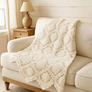 May include: A cream-colored crochet throw blanket featuring a repeating circular sunburst pattern. The blanket is constructed from interconnected yarn motifs, creating a textured, openwork design that drapes over the seat of a sofa.