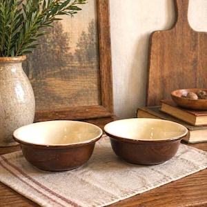 Peut inclure: Deux bols en céramique assortis présentant un extérieur émaillé brun foncé et un intérieur lisse de couleur crème. Les bols ont une forme arrondie avec un bord légèrement évasé, offrant un design simple et fonctionnel pour servir.