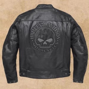 Può includere: Giacca da moto in pelle nera con logo Harley-Davidson a forma di teschio sul retro. La giacca ha un design classico con colletto rotondo, chiusura con cerniera e tasche multiple. Il logo Harley-Davidson è in un cerchio.