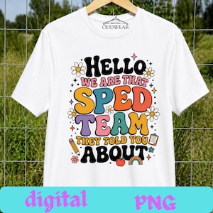 Può includere: T-shirt bianca con una grafica colorata che recita "Hello We Are That Sped Team They Told You About". Il design include margherite, una matita, una mela e un arcobaleno. La maglietta è appesa a una gruccia di legno.