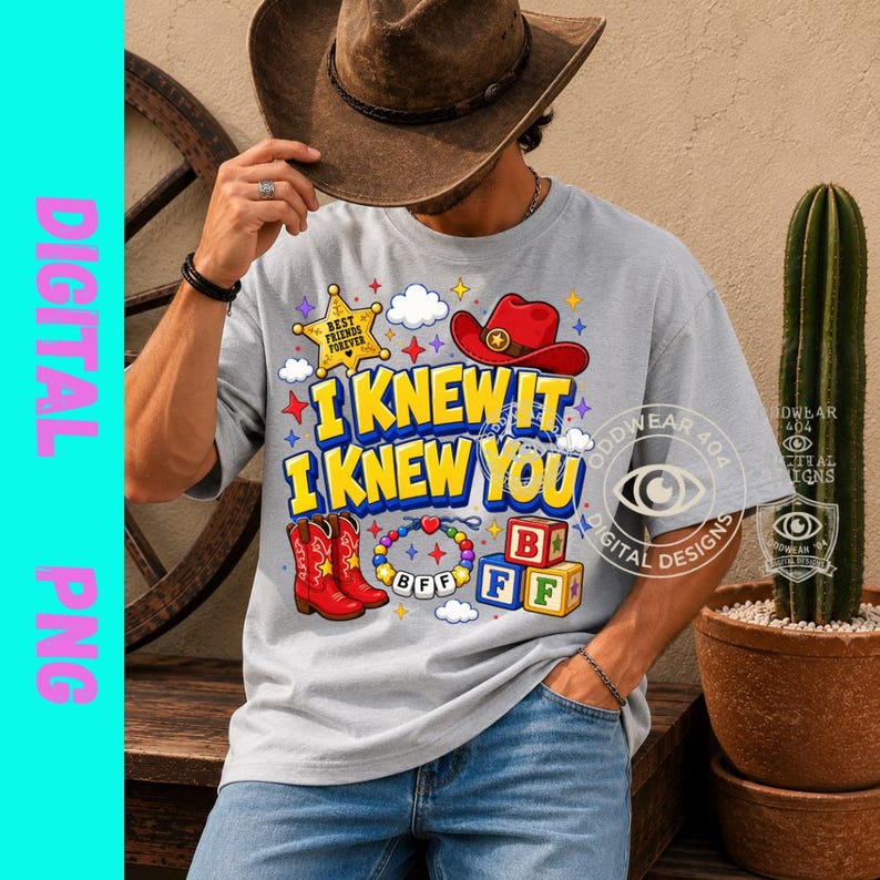 May include: A light gray t-shirt featuring a graphic print with the text I KNEW IT I KNEW YOU in yellow and blue. The design includes a yellow sheriff star, a red cowboy hat, red cowboy boots, a colorful beaded bracelet, and alphabet blocks.