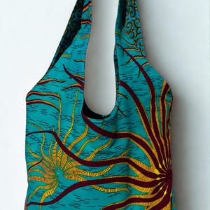 Peut inclure: Un sac fourre-tout turquoise avec un motif de soleil jaune et bordeaux. Le sac a une large ouverture et de longues anses. La doublure intérieure est bleu foncé avec un motif tourbillonnant. Parfait pour le shopping ou le transport quotidien.