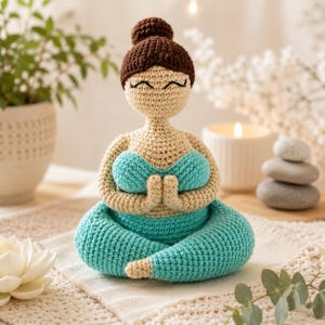 Pode incluir: Figura de ioga de crochê em pose sentada, com coque castanho, olhos fechados e tez clara. A figura usa sutiã e calças turquesa, com as mãos juntas em oração. A figura tem aproximadamente 15 cm de altura.