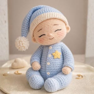 May include: A crocheted baby doll in a light blue onesie with a yellow star and a matching cap with a white brim and pom-pom. The doll has closed eyes and rosy cheeks, perfect for a nursery.