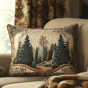 May include: Rectangular decorative pillow featuring a forest scene with evergreen trees, a path, and a light-colored sky. The pillow has a quilted design with a brown border and is placed on a beige sofa. The pillow's color palette includes greens, browns, and beige.