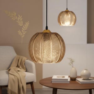 May include: Two pendant lights with amber-colored, ribbed glass shades hang from the ceiling. The larger light is in the foreground, with a smaller one in the background. The shades have a round shape and a gold-colored metal fixture.