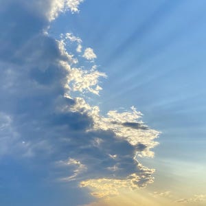 May include: A photograph of a partly cloudy sky. The sky is a gradient of blue, with the sun's rays breaking through the clouds. The clouds are white and gray, with some areas of sunlight.