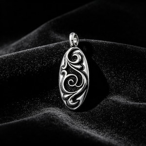Peut inclure: Pendentif ovale argenté avec un motif floral tourbillonnant orné. Le pendentif est doté d'une boucle pour une chaîne et est présenté sur un fond de velours noir. Le design présente des courbes et des motifs détaillés.