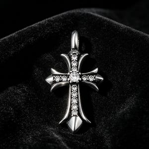 Op de afbeelding: Een zilverkleurige hanger in de vorm van een kruis, versierd met meerdere heldere edelstenen. Het kruis heeft een gedetailleerd ontwerp met puntige randen en een lus voor een ketting. De hanger is geplaatst tegen een donkere, getextureerde achtergrond.