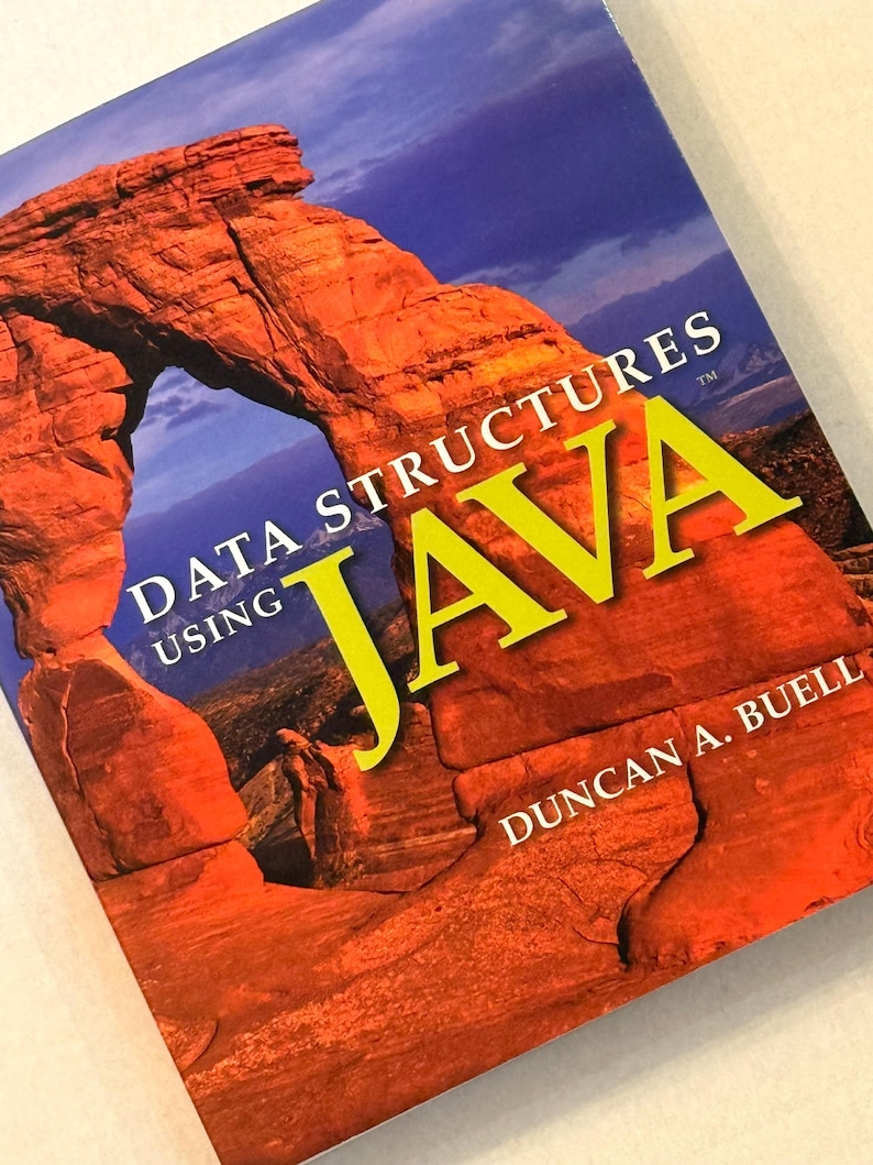 Pu&ograve; includere: Un libro di testo intitolato "Data Structures Using Java" di Duncan A. Buell. La copertina presenta un'immagine vibrante di una formazione rocciosa rossa sotto un cielo blu, con la parola "JAVA" in grandi lettere gialle.