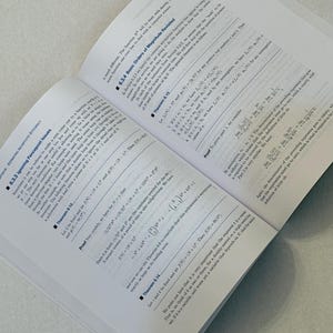 Pu&ograve; includere: Un libro di testo aperto con equazioni e teoremi matematici. Le pagine sono bianche con testo nero e il libro &egrave; angolato su una superficie grigio chiaro. Il libro &egrave; aperto a una sezione sull'efficienza asintotica economica.