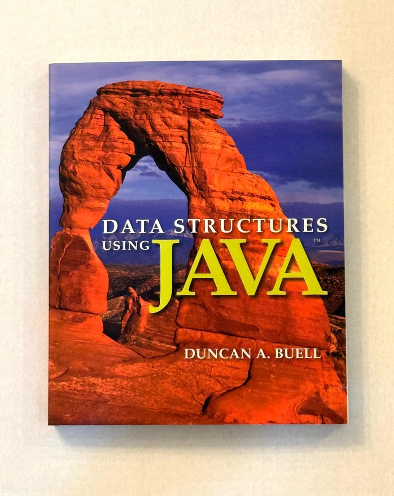 Pu&ograve; includere: Un libro intitolato "Data Structures Using Java" di Duncan A. Buell. La copertina presenta una fotografia di un arco di roccia rossa sotto un cielo blu. La parola "JAVA" &egrave; in grandi lettere gialle.