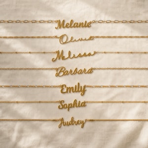 Könnte beinhalten: Sieben goldfarbene Halsketten, die horizontal angeordnet sind und jeweils einen anderen Namen in Schreibschrift tragen: Melanie, Olivia, Melissa, Barbara, Emily, Sophia und Audrey. Jede Kette hat ein einzigartiges Design, darunter Glieder- und Perlenketten.