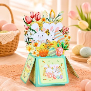May include: A 3D pop-up greeting card featuring a festive Easter scene with white bunnies, yellow ducklings, colorful patterned eggs, and spring flowers like tulips and daffodils. The base is a light green box with bunny illustrations.