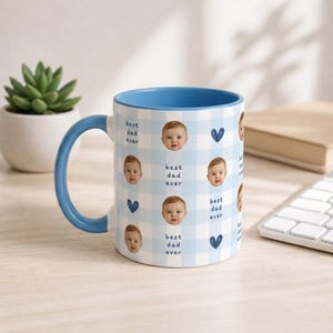 Puede incluir: Una taza de cerámica a cuadros azules y blancos con asa e interior azules. La taza está decorada con fotos de bebés, corazones azules y el texto "best dad ever". Una planta suculenta y un teclado están en el fondo.