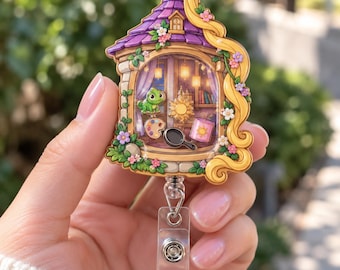 May include: A decorative badge reel featuring a tower-shaped design with a purple roof and long blonde hair. The center shows a window scene with a green lizard, a paint palette, a frying pan, and a sun emblem surrounded by small flowers.