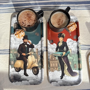 May include: Two serving trays with a vintage illustration of a man on a scooter and a woman holding a car. Each tray holds a black mug of coffee and a cookie. The background features a cityscape and clouds.