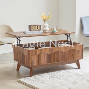 May include: A rectangular wooden coffee table with a lift-top mechanism, featuring a fluted front panel with a scalloped upper edge and four tapered legs. The table surface holds a vintage-style radio, a book, and a small floral vase.