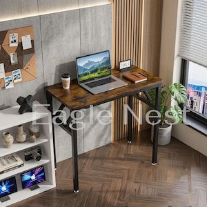 May include: A rectangular desk with a dark wood grain surface and a black metal frame. A silver laptop is open on the desk next to a brown notebook and a disposable coffee cup. The desk is positioned in a room with a white bookshelf nearby.