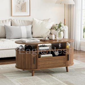 May include: A walnut-toned oval coffee table featuring a central open shelf, two side cabinets with vertical slat doors, and a central drawer with a woven rattan panel. The table has four tapered legs and holds books, a teapot, and decor.