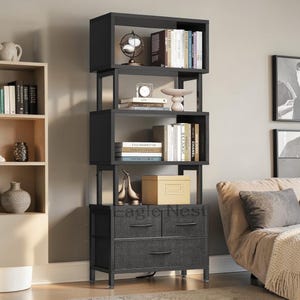 May include: A black bookshelf with open shelves and two drawers. The shelves display books, decorative objects, and a globe. The drawers have dark gray fabric fronts and black handles. The text "Eagle Nest" is visible on the front.