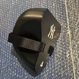May include: A black foam knee pad featuring the white New York Yankees logo and the number 4 printed on the side. The protective gear includes a black adjustable fabric strap with a hook and loop fastener for secure attachment during use.