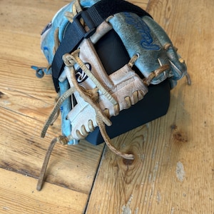 May include: A weathered light blue and white leather baseball glove featuring tan leather lacing, a black adjustable strap across the back, and the Rawlings brand logo embroidered in blue on the outer thumb section of the glove.