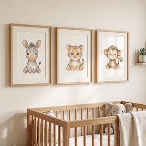 Pode incluir: Três impressões emolduradas para berçário com ilustrações em aquarela de uma zebra, um tigre e um macaco. As impressões estão em molduras de madeira clara e são exibidas acima de um berço de madeira com um elefante de pelúcia e um cobertor.