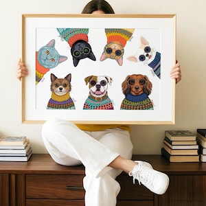 May include: A framed art print featuring illustrated cats and dogs wearing colorful sweaters and sunglasses. The animals are depicted in a whimsical style, with each animal's name written on the print. The frame is a light brown color.