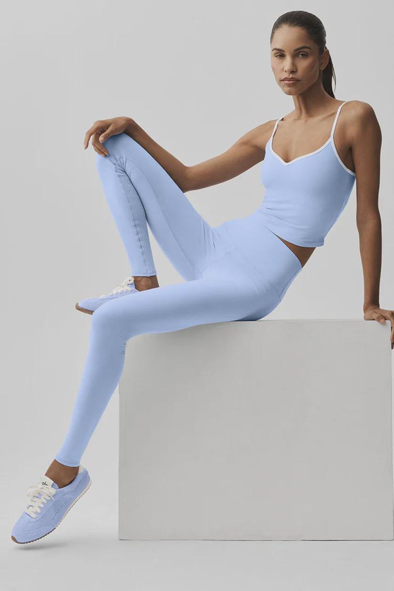 May include: A light blue athletic outfit comprising a vest top with white trim and matching leggings. The model is also wearing light blue trainers with white laces. The outfit is designed for fitness activities.