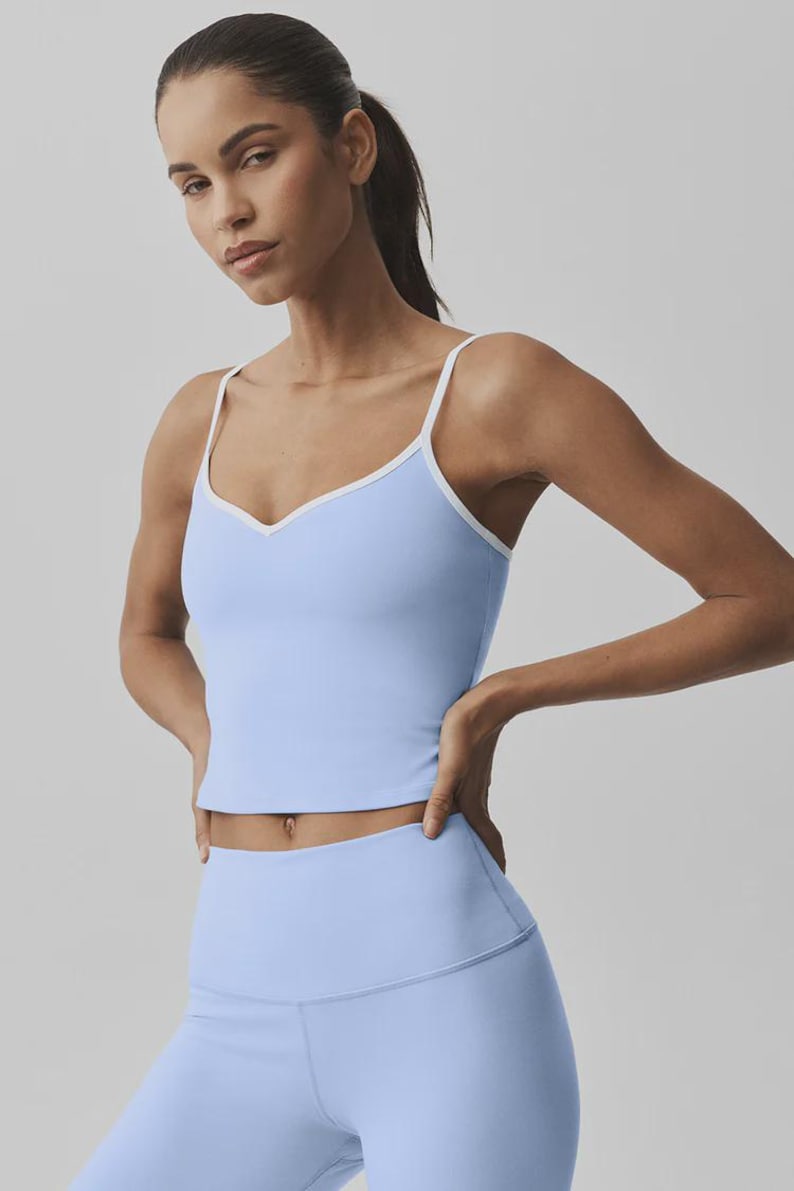 May include: Pale blue camisole top with white trim and matching leggings. The camisole has a V-neck and thin straps. The outfit is made of a soft, stretchy material, suitable for yoga or other activities.