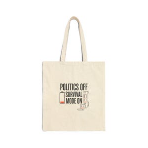 May include: Cream-colored tote bag with the text "POLITICS OFF SURVIVAL MODE ON" in black. The design includes a low battery icon and a stack of papers. The bag has two long handles for carrying.