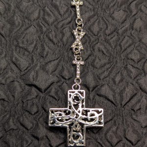 May include: A silver-toned necklace featuring a large, ornate cross pendant with intricate filigree cutouts. The chain is adorned with smaller cross-shaped links and an X-shaped link, all encrusted with small, clear, sparkling rhinestones.