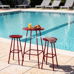 May include: A tall, round, red metal bistro table with four thin legs and a square footrest, accompanied by two matching red metal bar stools. A glass of orange juice and a plate with two croissants sit on the table surface. Text reads HavenNestDecor.