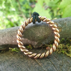 May include: A circular ring crafted from twisted copper wire, featuring a polished metallic finish. A small, black cord is looped through the top section of the ring, providing a contrast to the warm, reddish-brown tones of the copper metal.