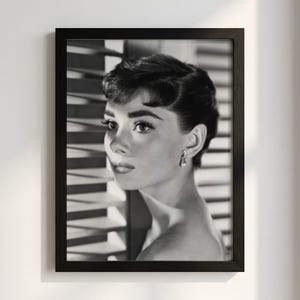 May include: A black and white framed portrait of a person with short dark hair, wearing a small dangling earring. The subject is positioned in profile, looking toward the left, with horizontal window blinds visible in the background.