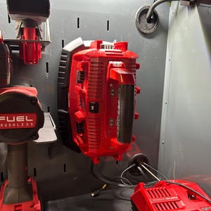 May include: Red power tools and accessories, including a drill, charger, and a large battery pack, are mounted on a gray metal surface. The tools are part of the FUEL brushless series. The image showcases a well-organized setup for power tool storage and charging.