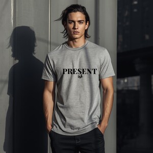 May include: A heather gray short-sleeved t-shirt featuring the text "PRESENT ish" printed in black across the chest. The shirt has a crew neckline and a standard fit, constructed from a soft, lightweight fabric with a subtle heathered texture.