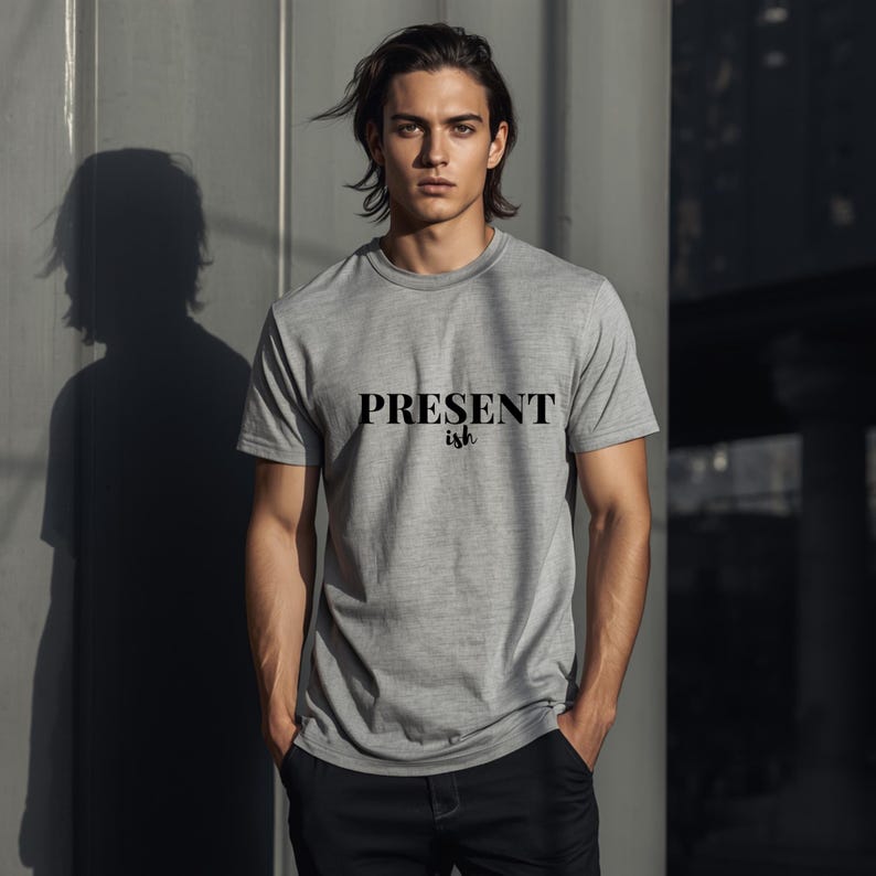 May include: A heather gray short-sleeved t-shirt featuring the text "PRESENT ish" printed in black across the chest. The shirt has a crew neckline and a standard fit, constructed from a soft, lightweight fabric with a subtle heathered texture.