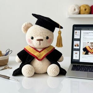 Puede incluir: Un oso de peluche tejido a ganchillo con birrete y toga de graduación. El oso es de color crema con birrete y toga negros, y una borla dorada. El oso tiene mejillas sonrosadas y está sentado junto a un portátil que muestra un patrón. Una cesta de hilo y herramientas de ganchillo están en el fondo.