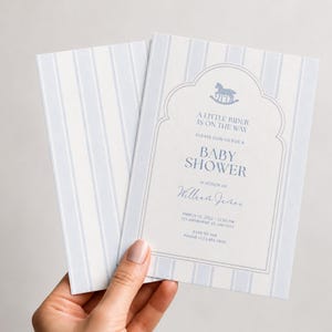 Puede incluir: Una tarjeta de invitación rectangular para baby shower con un patrón de rayas verticales en azul claro y blanco. El centro incluye un marco de arco decorativo, un icono de caballo mecedora y el texto A LITTLE RIDER IS ON THE WAY.
