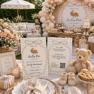 Puede incluir: Una mesa de baby shower con dos tarjetas impresas con una ilustración de tarta y el texto A Sweet Little Cutie Pie Is On The Way, un oso de peluche beige, patucos de punto, una tarta pequeña y un ramo de flores en tonos melocotón y blanco.