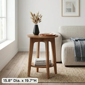 May include: A round wooden side table with a lower shelf. The table has a diameter of 15.8 inches and is 19.7 inches high. A black vase with dried flowers sits on top. The shelf holds books with the text "DESIGN AS ART", "MINIMALIST FORMS", and "THE SCANDI HOME".