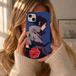 May include: A blue phone case featuring an anime character with black hair and a gray cloak. The case has a red cloud design and a black sword. The phone case is held up by a person.