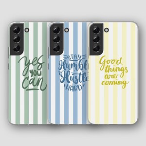 Op de afbeelding: Drie telefoonhoesjes met verticale streepontwerpen in groen, blauw en geel. Elke hoes heeft een ander motiverend citaat in een handschriftstijl: "Yes you can", "Stay Humble Hustle Hard" en "Good things are coming".