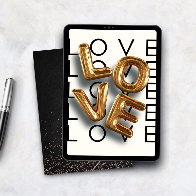 May include: A tablet displays the word "LOVE" in gold, balloon-style letters against a black and white background. A black notebook and a silver pen are next to the tablet. The image has a clean, modern aesthetic.