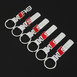 May include: A collection of silver-colored metal keychains with red accents. Each keychain features a different model designation, including "RS6", "S-line", "SQ5", "S4", and "S6". The keychains have a circular key ring.